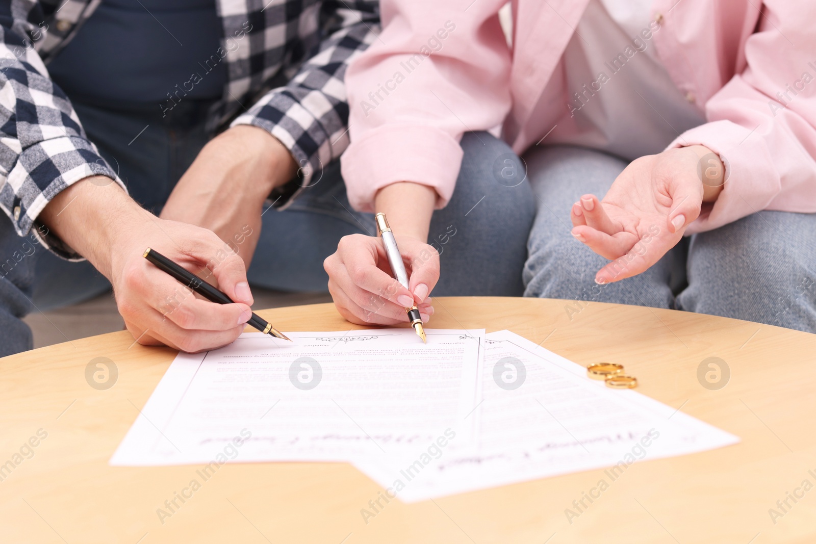 Photo of Man and woman signing marriage contract at wooden table indoors, closeup