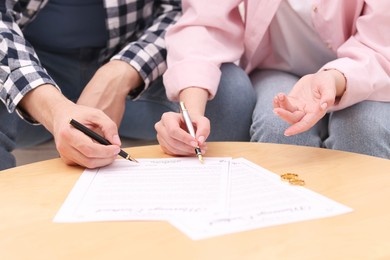 Man and woman signing marriage contract at wooden table indoors, closeup