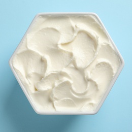 Bowl of tasty cream cheese on color background, top view