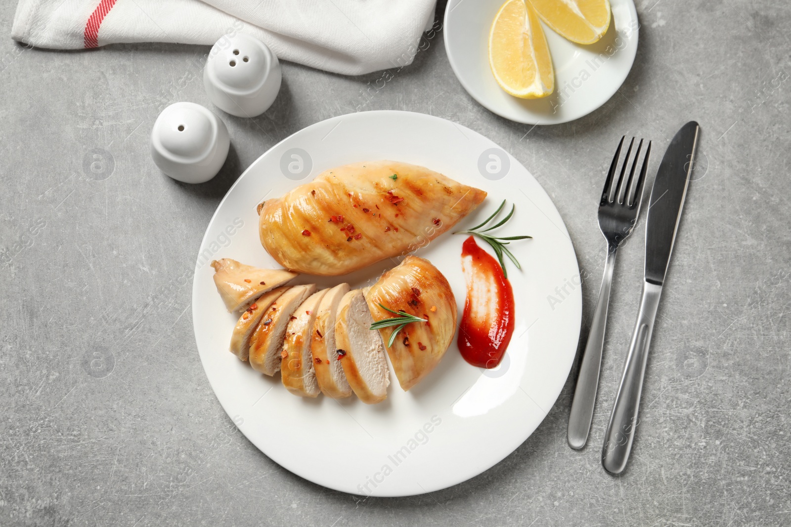 Photo of Fried chicken breasts served with sauce and lemon on grey table, top view