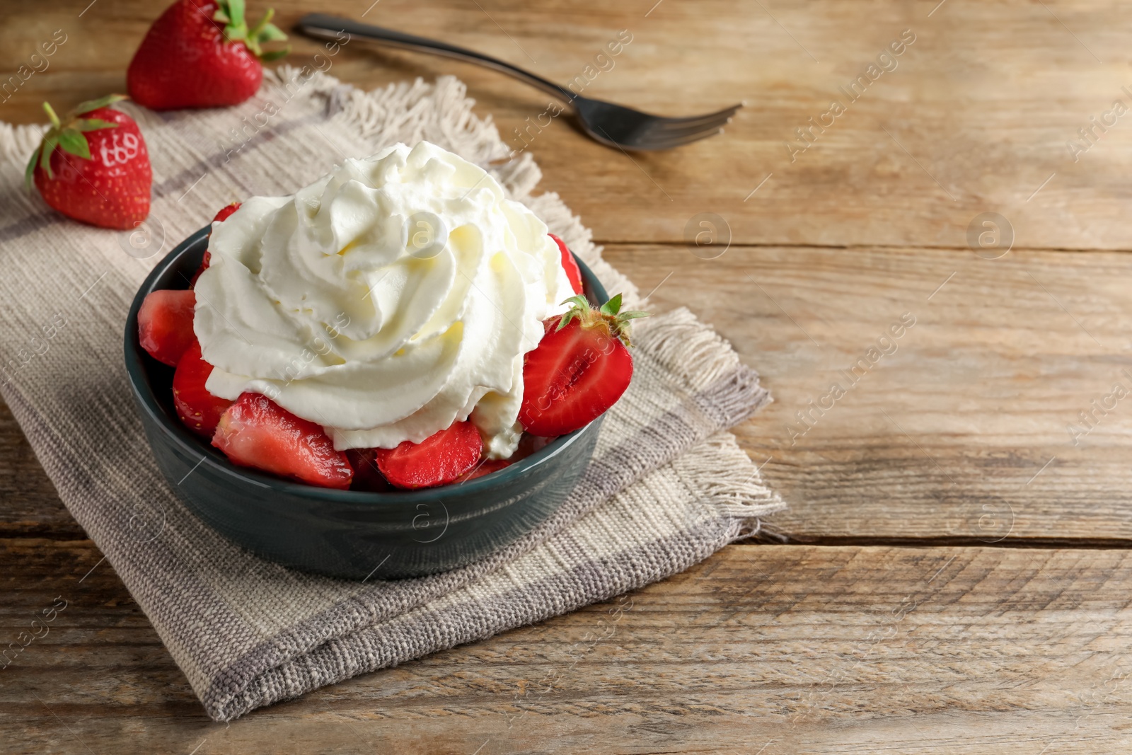 Photo of Bowl with delicious strawberries and whipped cream served on wooden table, space for text