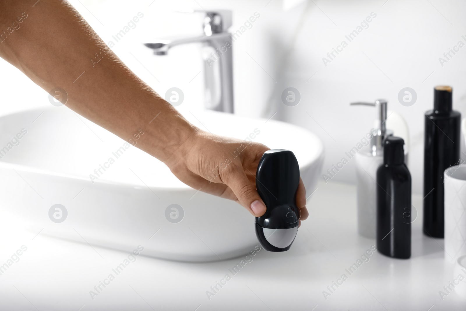 Photo of Man holding roll-on deodorant in bathroom, closeup view