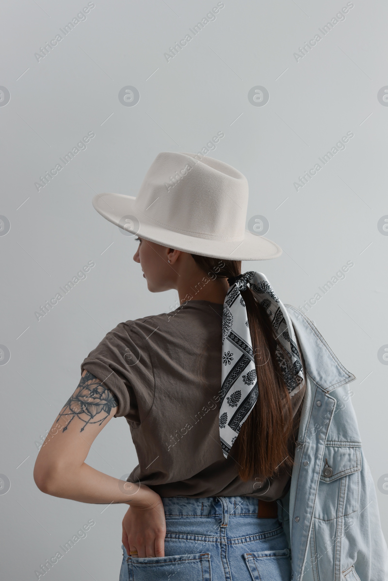 Photo of Young woman with hat and stylish bandana on light background, back view