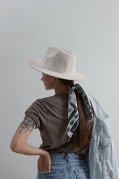 Young woman with hat and stylish bandana on light background, back view
