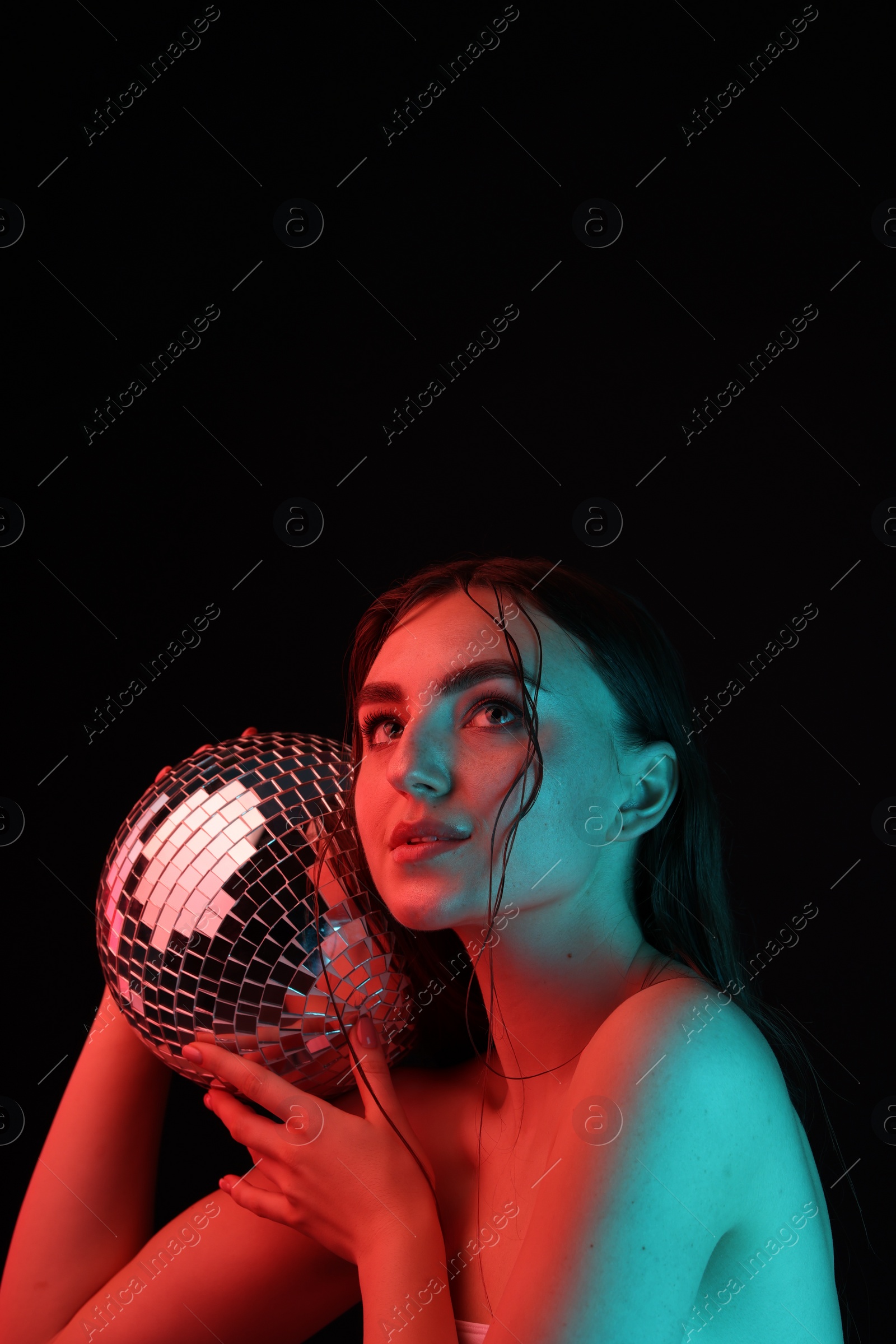 Photo of Beautiful woman with disco ball posing in neon lights against black background