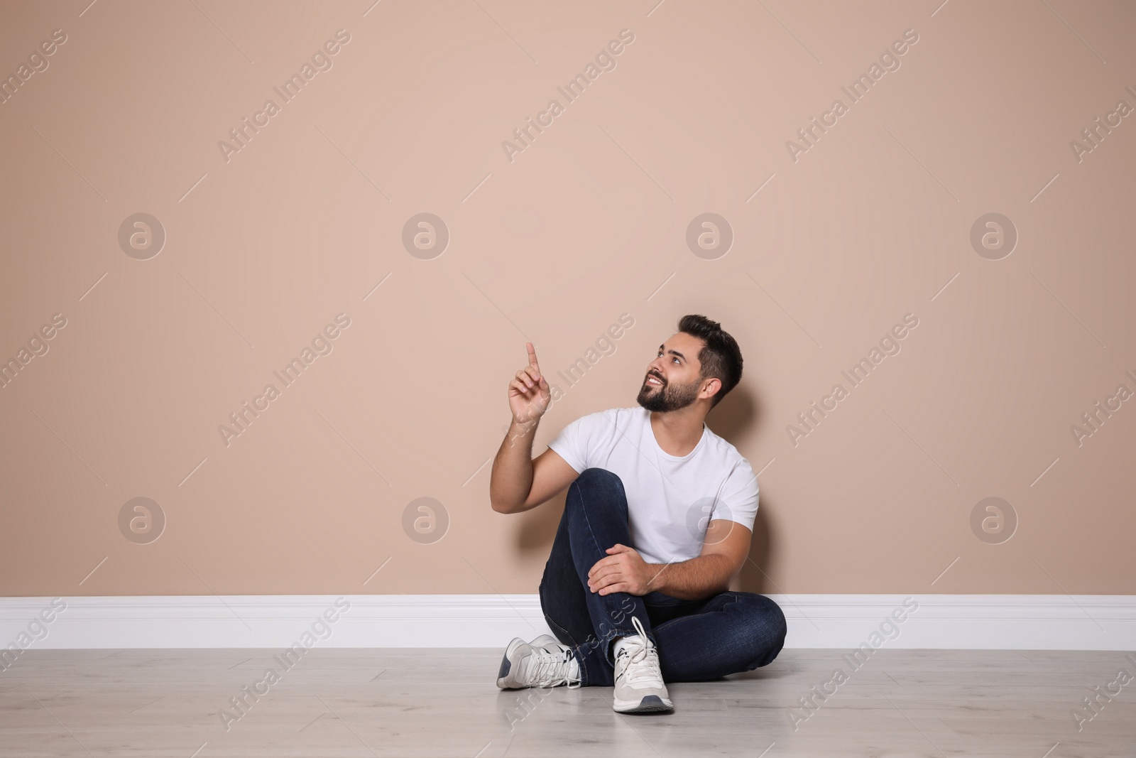Photo of Young man sitting on floor near beige wall indoors
