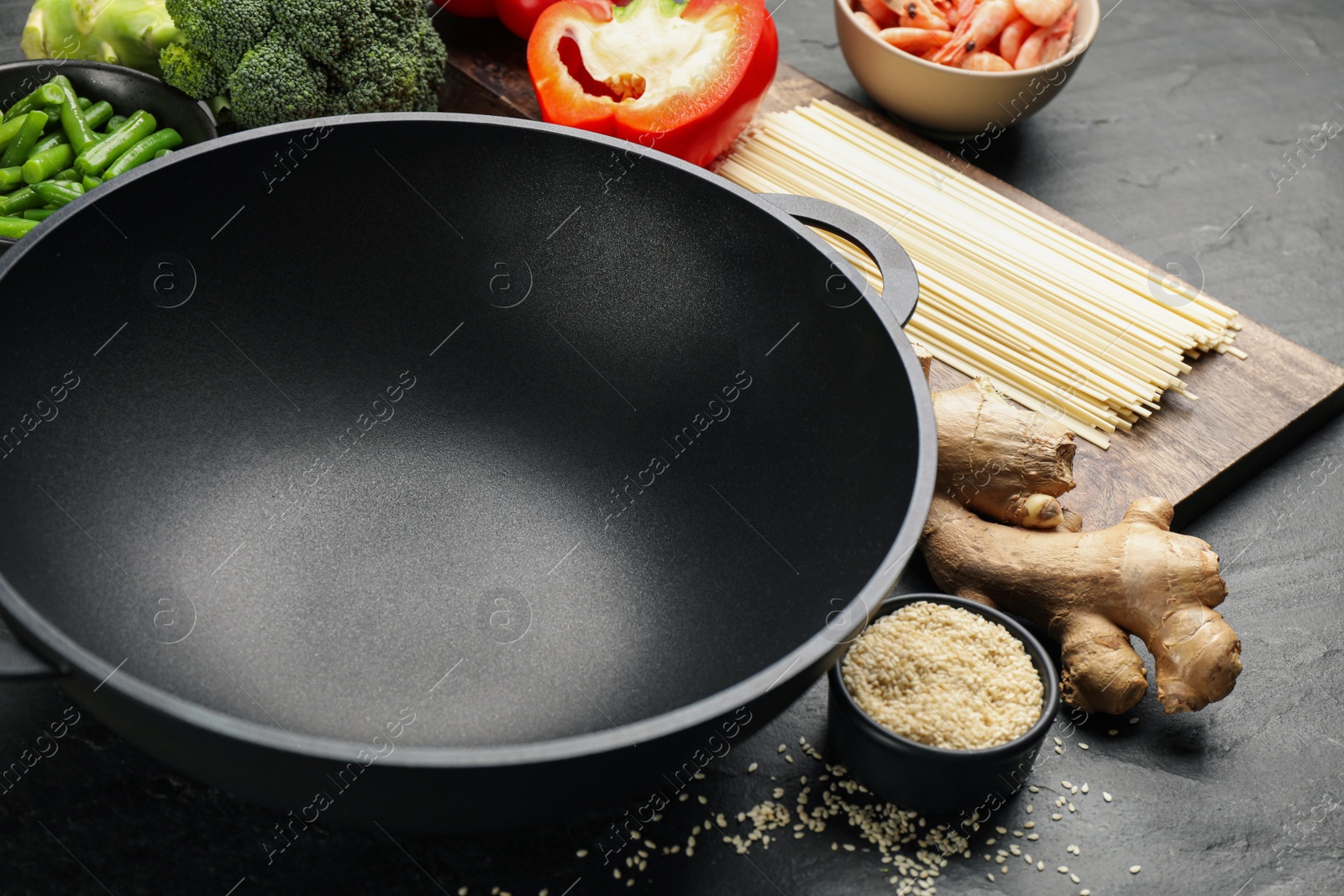 Photo of Empty iron wok and raw ingredients on black table, closeup