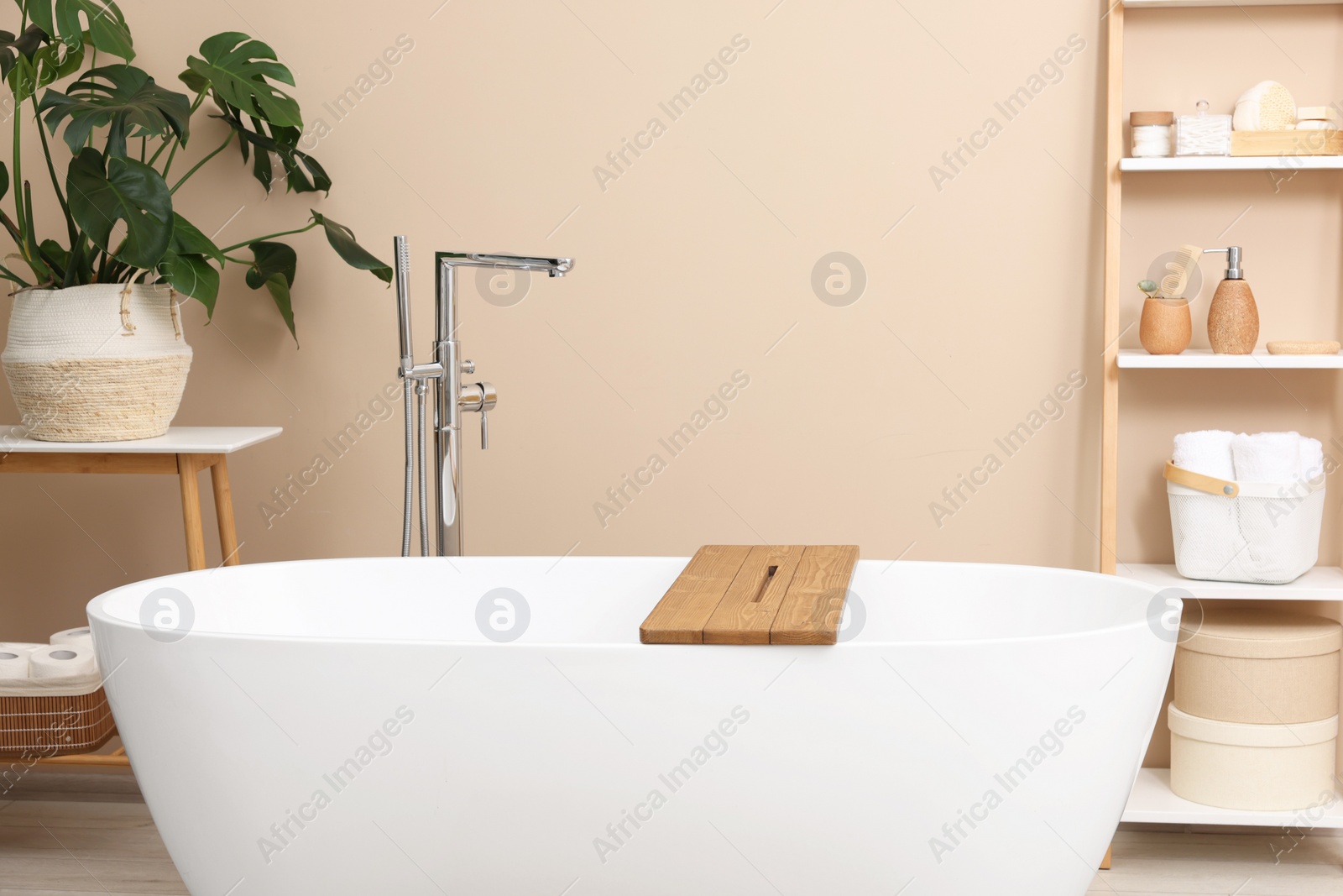 Photo of Bath tub with wooden board and different personal care products and accessories on shelving unit in bathroom