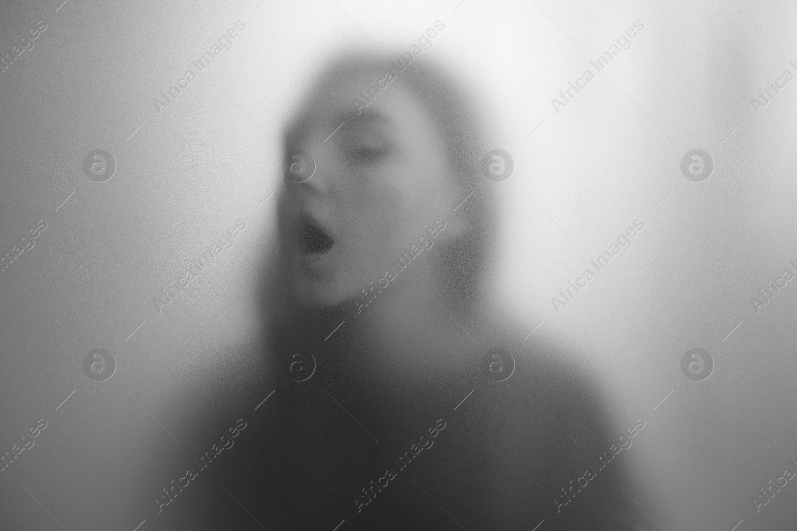 Photo of Silhouette of ghost behind fabric against light grey background. Black and white effect