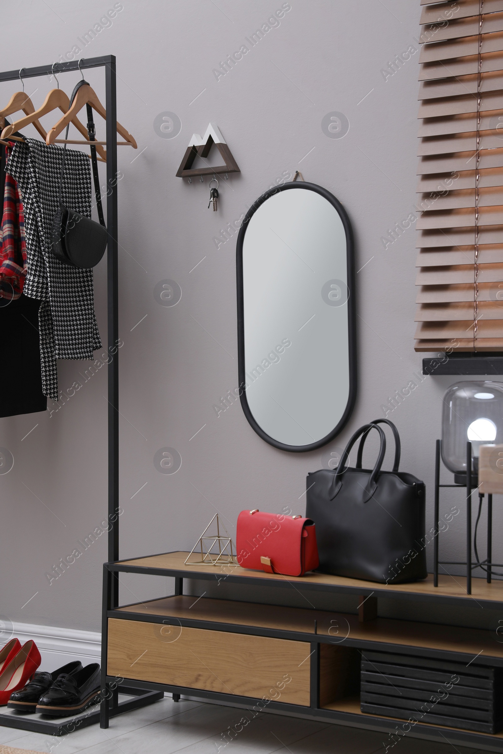 Photo of Modern hallway interior with stylish furniture, mirror and wooden hanger for keys on grey wall