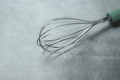 Photo of Metal whisk on gray table, closeup. Kitchen tool