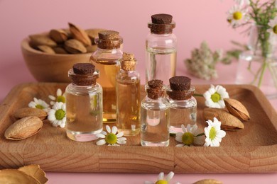 Photo of Aromatherapy. Different essential oils, flowers and almonds on pink background