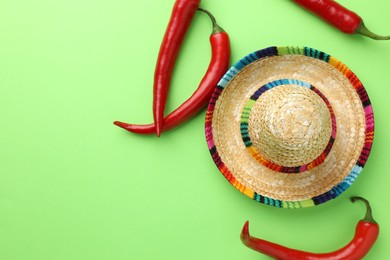 Photo of Mexican sombrero hat and chili peppers on green background, flat lay. Space for text