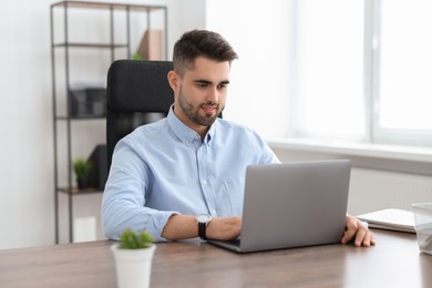 Photo of Happy young programmer working with laptop in office