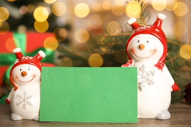 Photo of Christmas composition with decorative snowman near blank green card on table, space for text