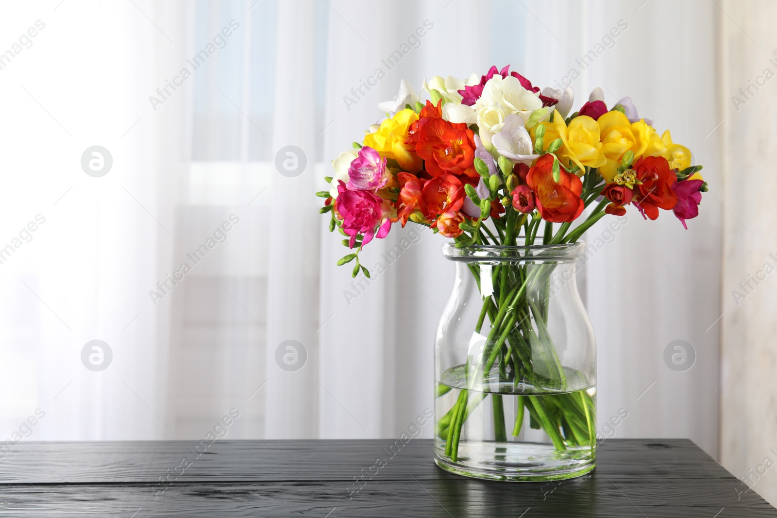 Photo of Vase with bouquet of spring freesia flowers on table in room. Space for text