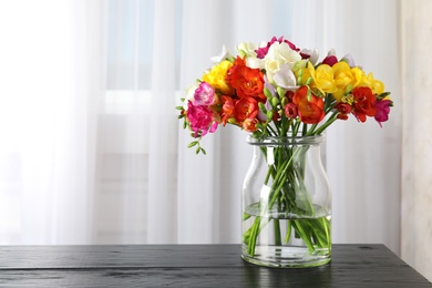 Photo of Vase with bouquet of spring freesia flowers on table in room. Space for text