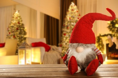 Image of Funny Christmas gnome on wooden table in room with festive decorations. Space for text