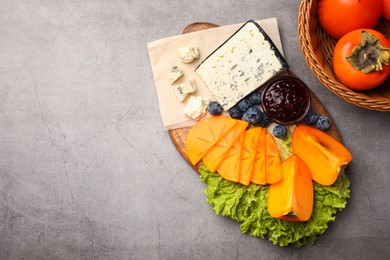 Photo of Delicious persimmon, blue cheese, blueberries and jam served on light grey table, flat lay. Space for text