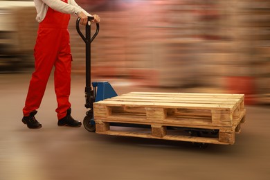 Image of Worker moving wooden pallets with manual forklift in warehouse, closeup