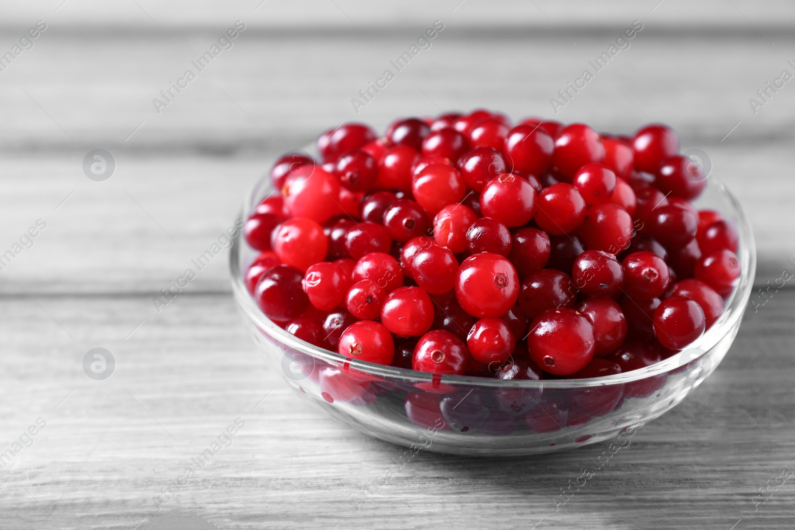 Photo of Fresh ripe cranberries in bowl on grey wooden table, closeup