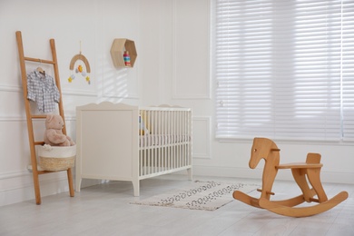 Cute baby room interior with comfortable crib and wooden rocking horse