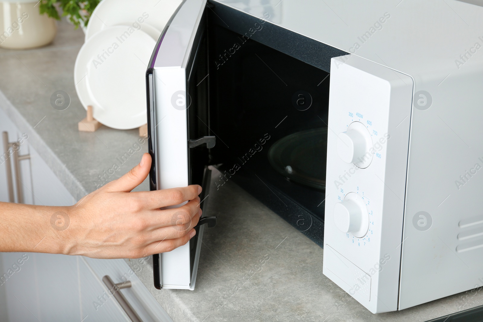 Photo of Woman opening microwave oven in kitchen, closeup