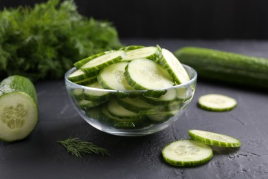 Cut cucumber in glass bowl on dark gray textured table, closeup