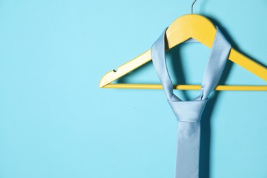 Photo of Hanger with silk tie on light blue background. Space for text