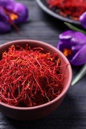 Dried saffron in bowl and crocus flowers on table, closeup