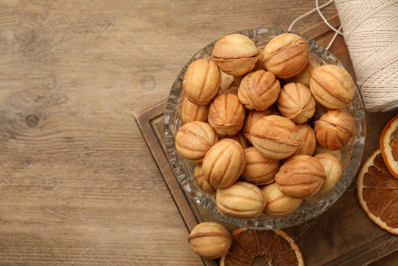 Photo of Bowl of delicious nut shaped cookies and dried orange slices on wooden table, flat lay. Space for text