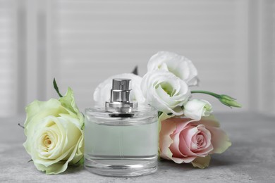 Photo of Bottle of perfume and flowers on grey table indoors