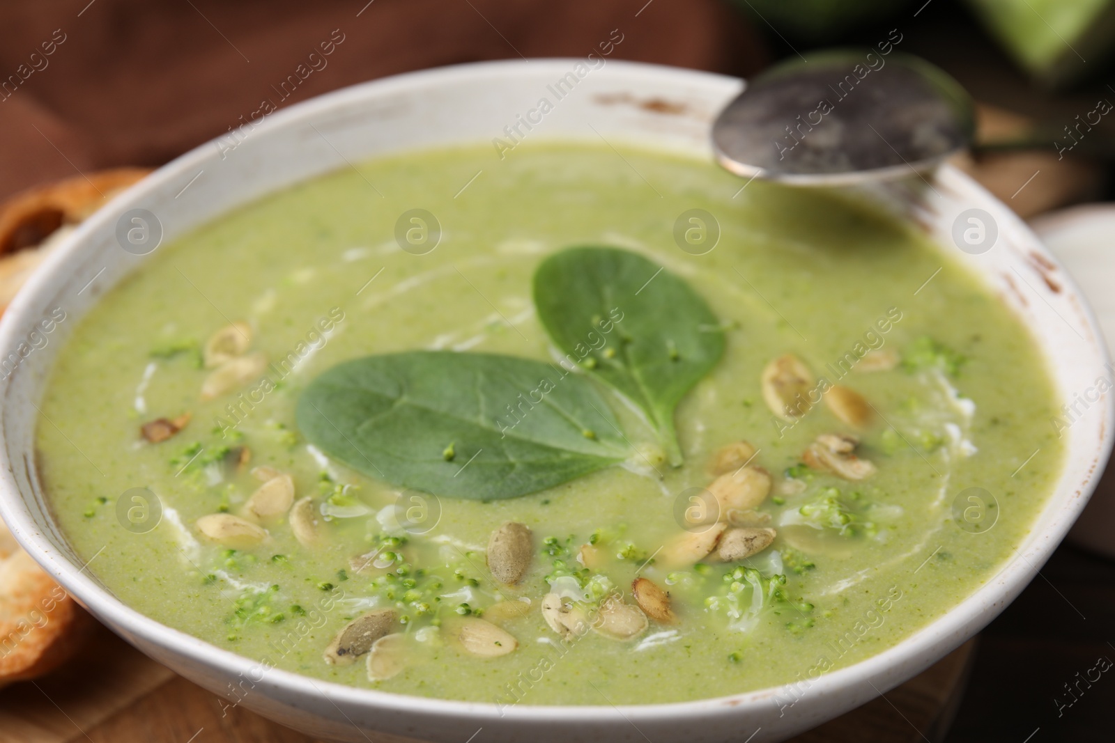 Photo of Delicious broccoli cream soup with basil and pumpkin seeds served on wooden table, closeup