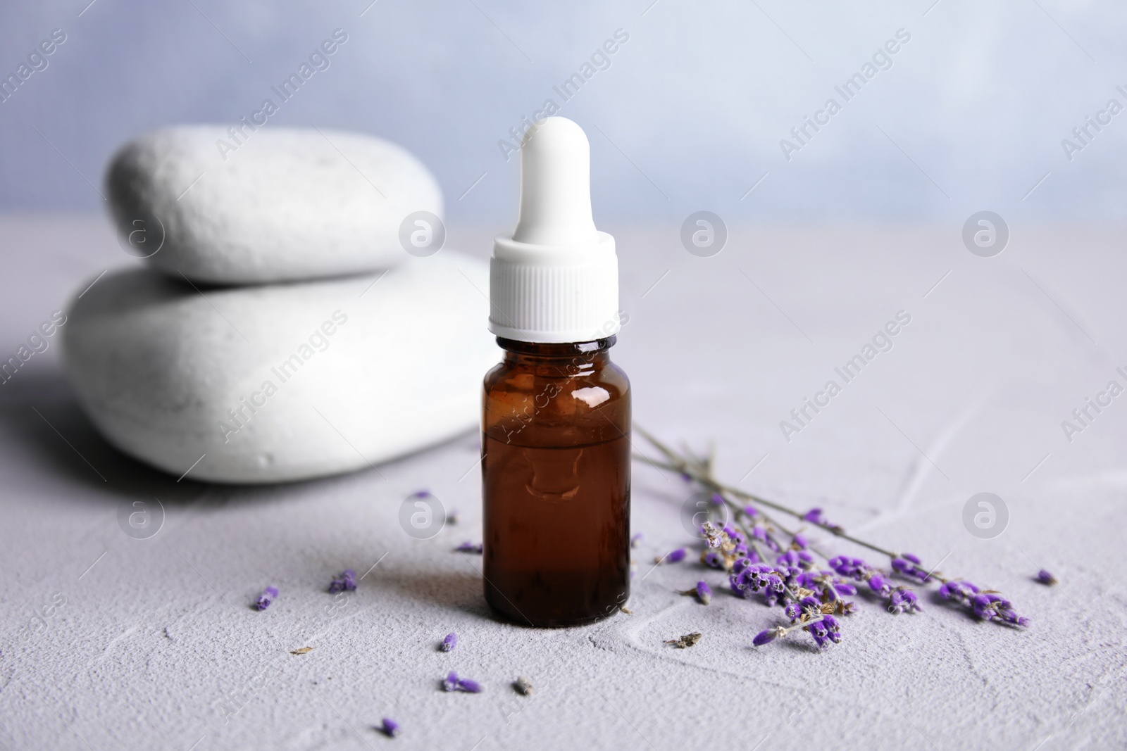 Photo of Natural herbal oil and lavender flowers on table against blurred background