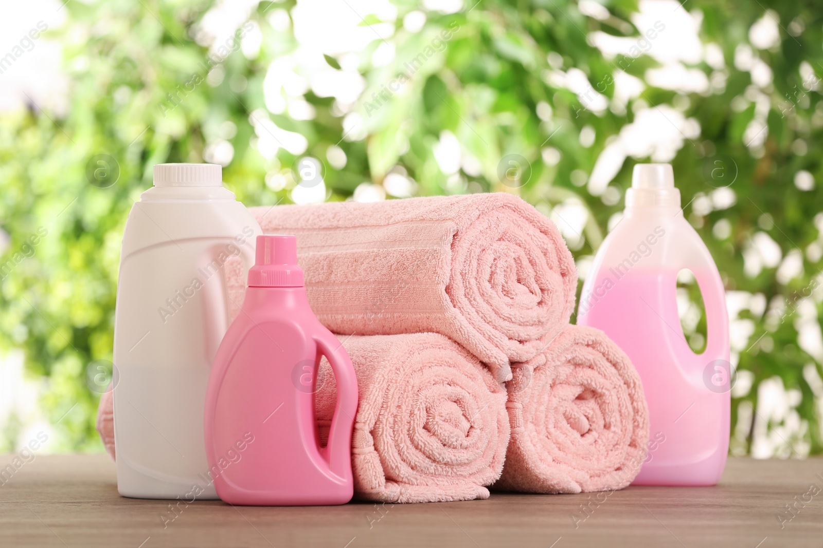 Photo of Rolled towels and detergents on wooden table against blurred background