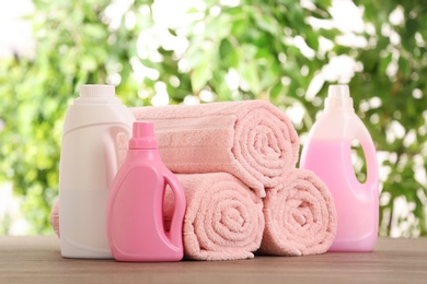 Rolled towels and detergents on wooden table against blurred background