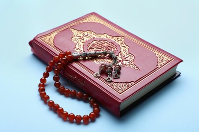 Photo of Muslim prayer beads and Quran on light blue background