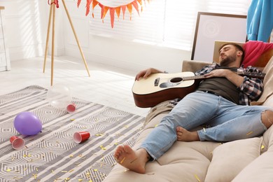 Young man with guitar sleeping on sofa in messy room after party