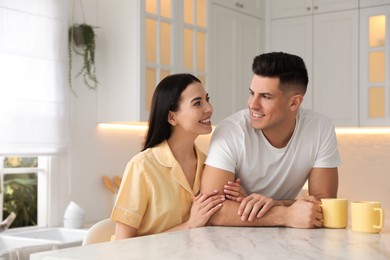 Photo of Happy couple wearing pyjamas at table in kitchen