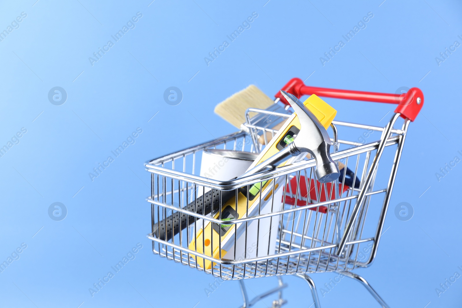 Photo of Small shopping cart with paint and renovation equipment on light blue background