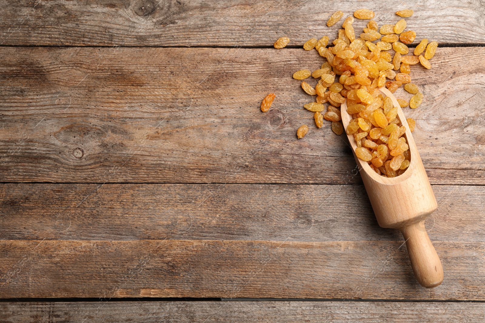 Photo of Scoop with raisins and space for text on wooden background, top view. Dried fruit as healthy snack