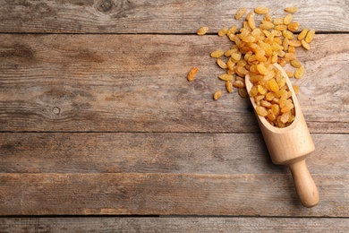 Scoop with raisins and space for text on wooden background, top view. Dried fruit as healthy snack