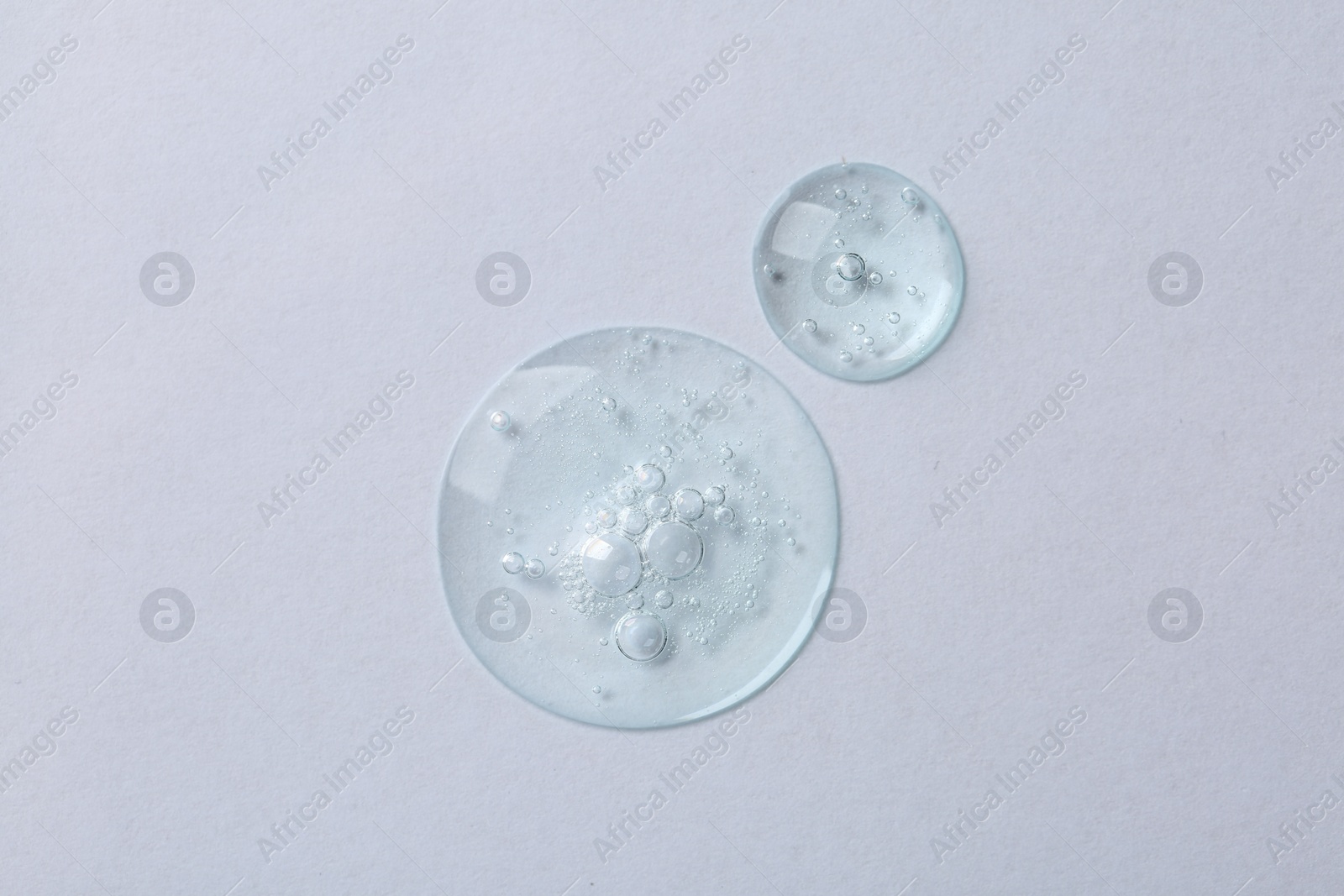 Photo of Drops of cosmetic serum on white background, top view