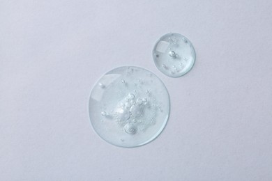 Photo of Drops of cosmetic serum on white background, top view