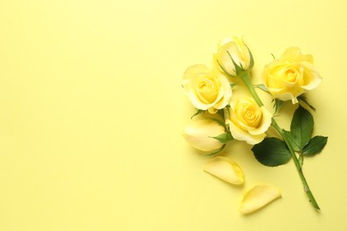 Beautiful roses and petals on yellow background, flat lay. Space for text