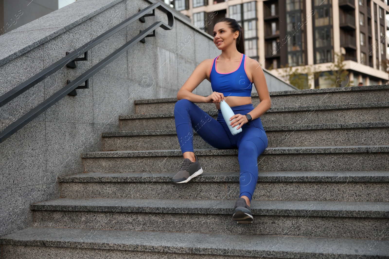 Photo of Beautiful woman in stylish sportswear with bottle of drink on stairs outdoors