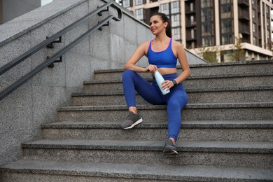 Photo of Beautiful woman in stylish sportswear with bottle of drink on stairs outdoors
