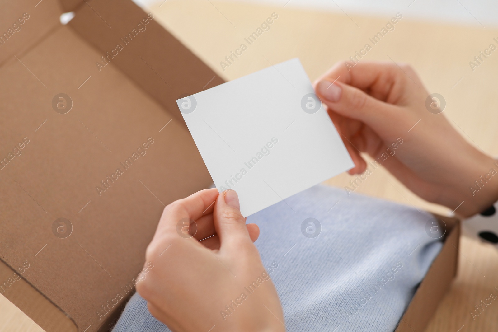 Photo of Woman holding greeting card near parcel with Christmas gift, closeup