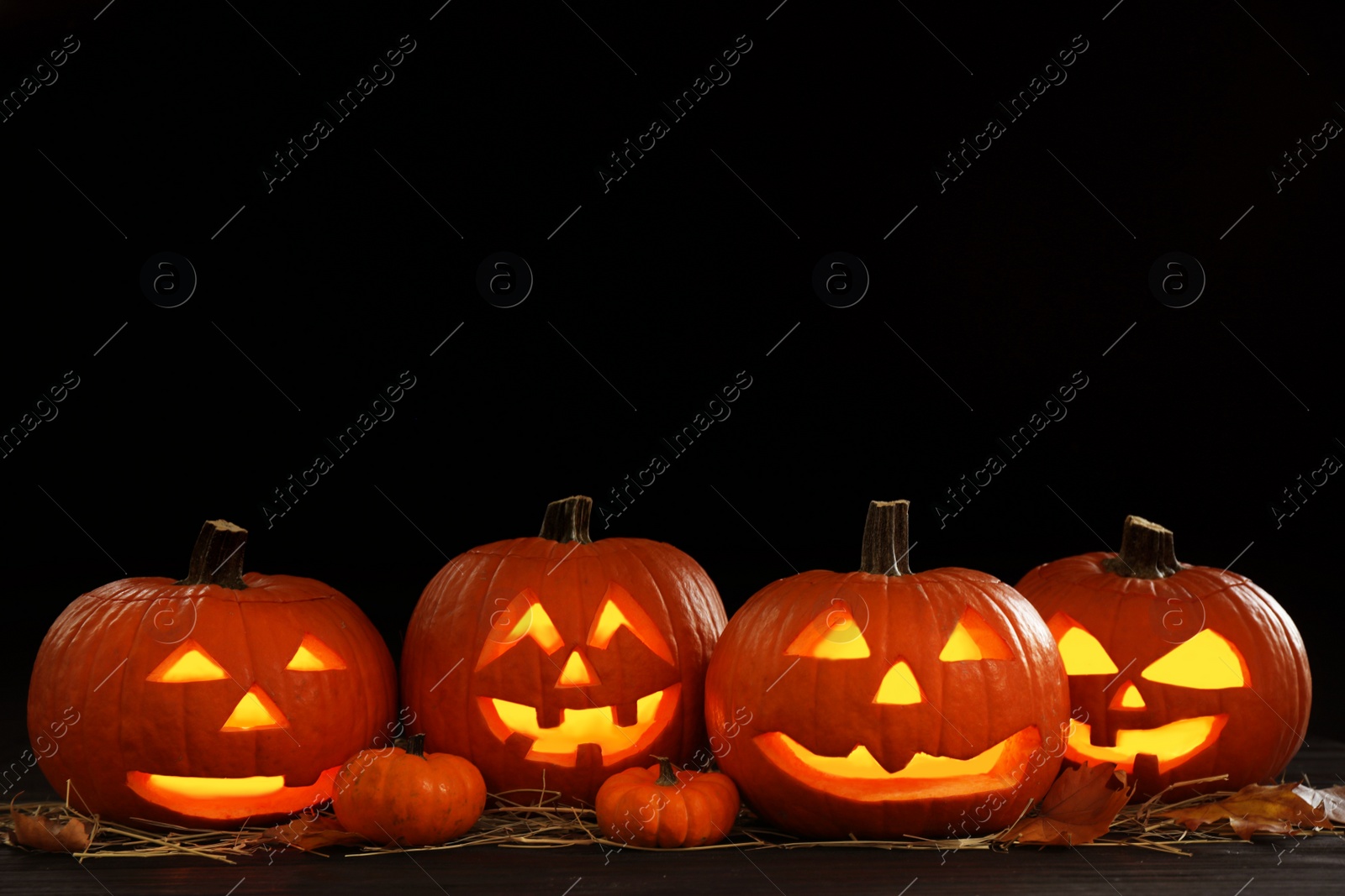 Photo of Glowing jack o'lanterns on table in darkness, space for text. Halloween decor