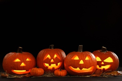 Photo of Glowing jack o'lanterns on table in darkness, space for text. Halloween decor